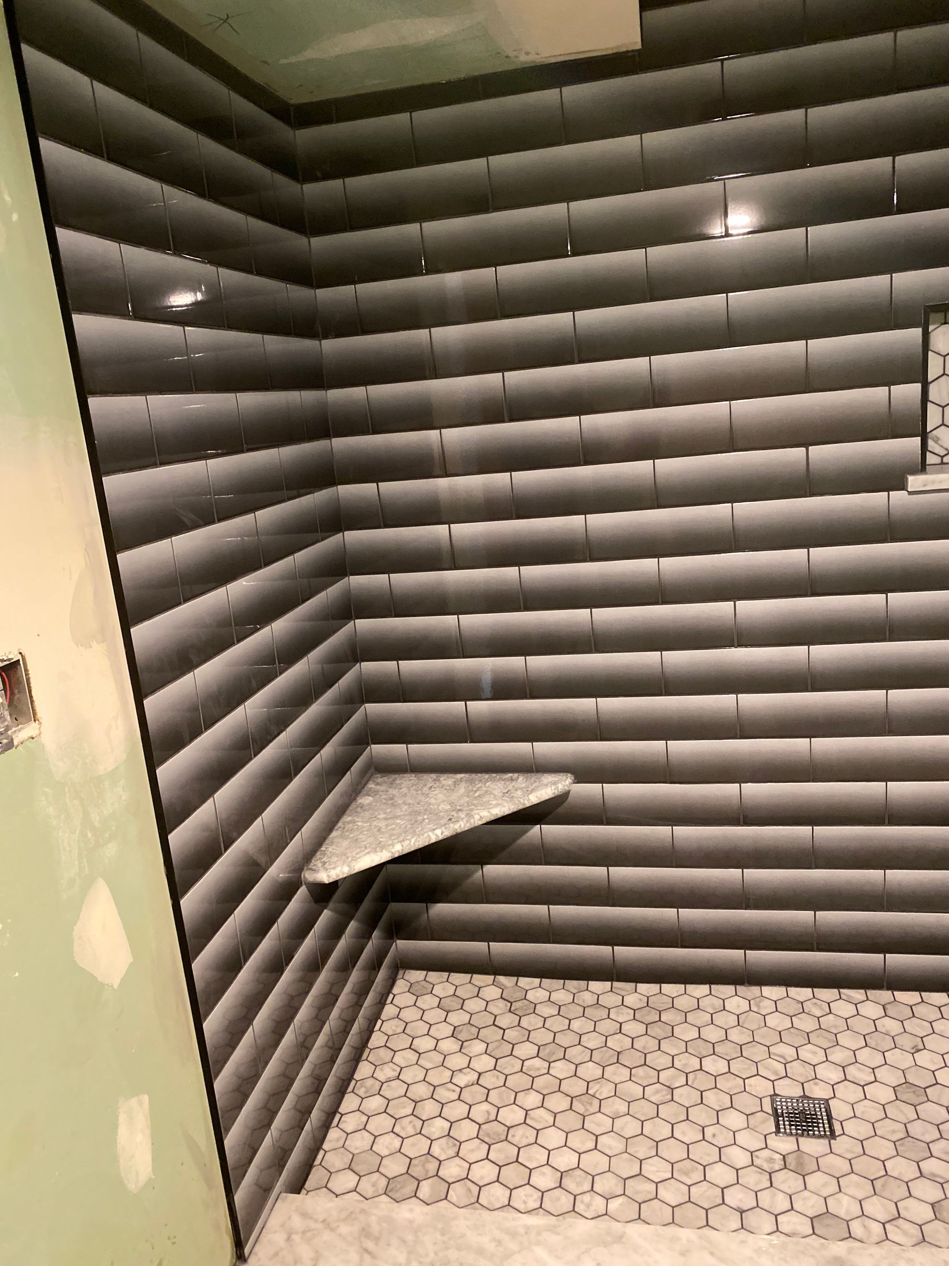Small tiled shower stall with gray wall panels, hexagon floor tiles, and a built-in bench.