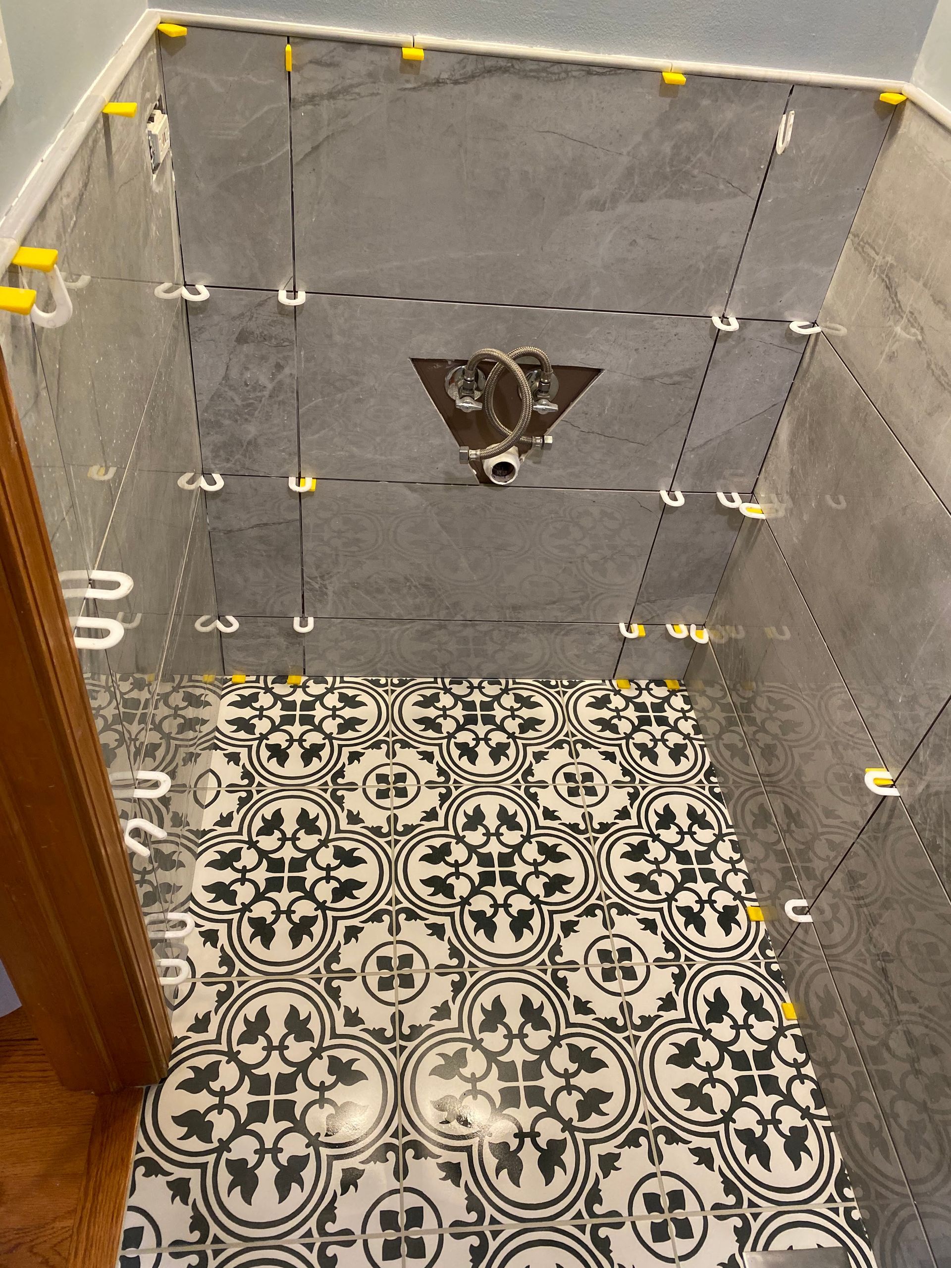 Small tiled shower stall with gray walls, patterned black-and-white floor, and a wall-mounted drain cover.