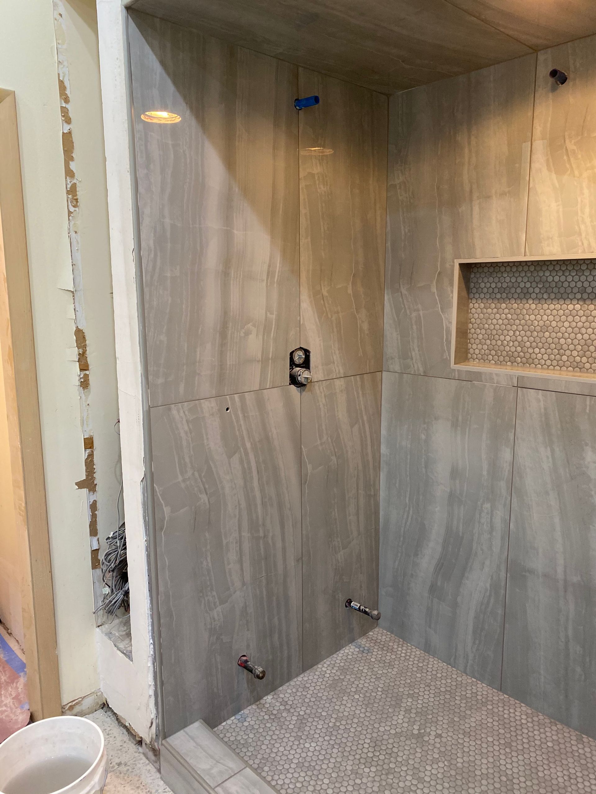 Tiled shower stall with unfinished gray walls, built-in niche, and plumbing fixtures