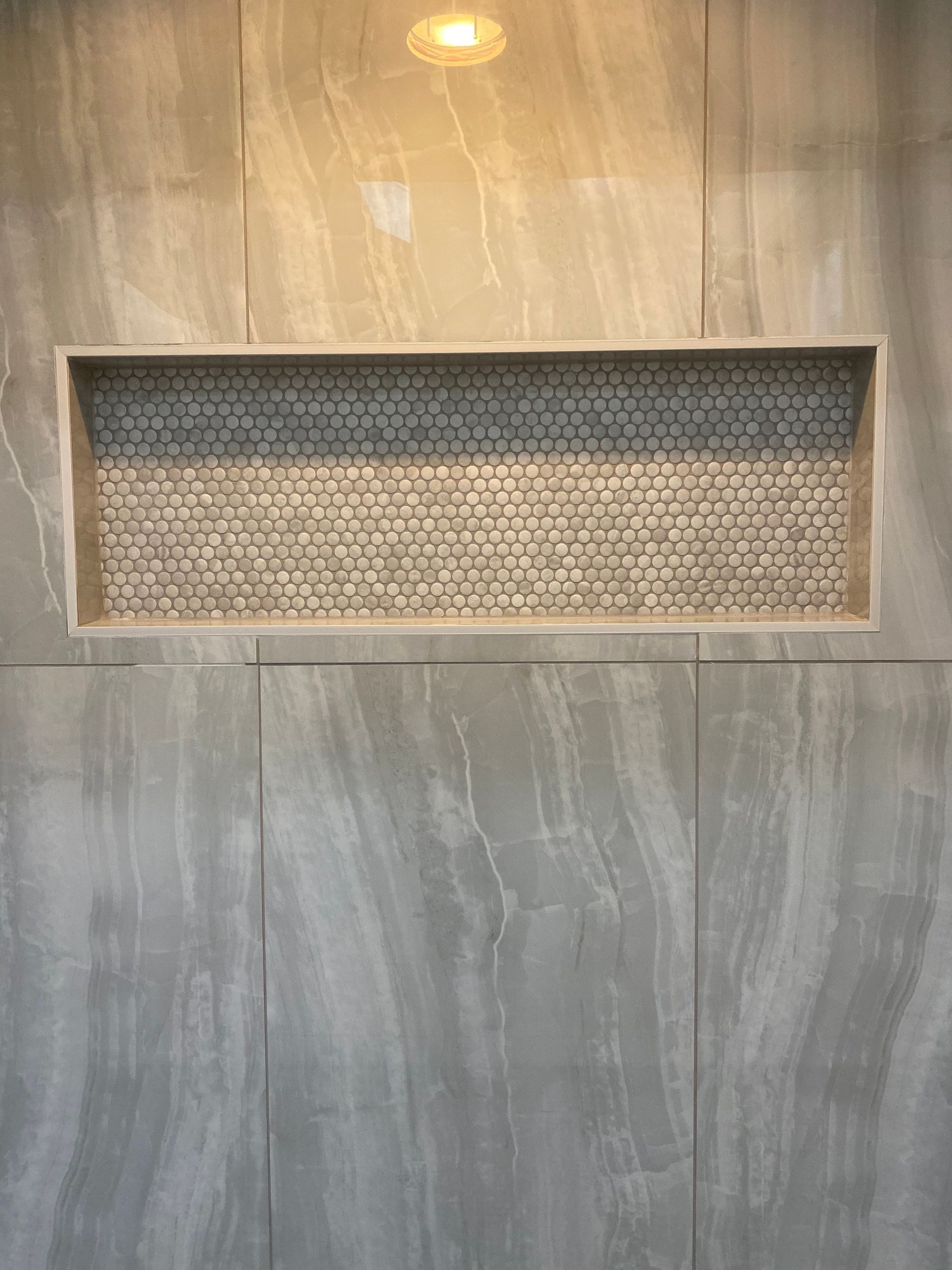 Gray tiled wall with a recessed rectangular mesh vent and a ceiling light reflection above it