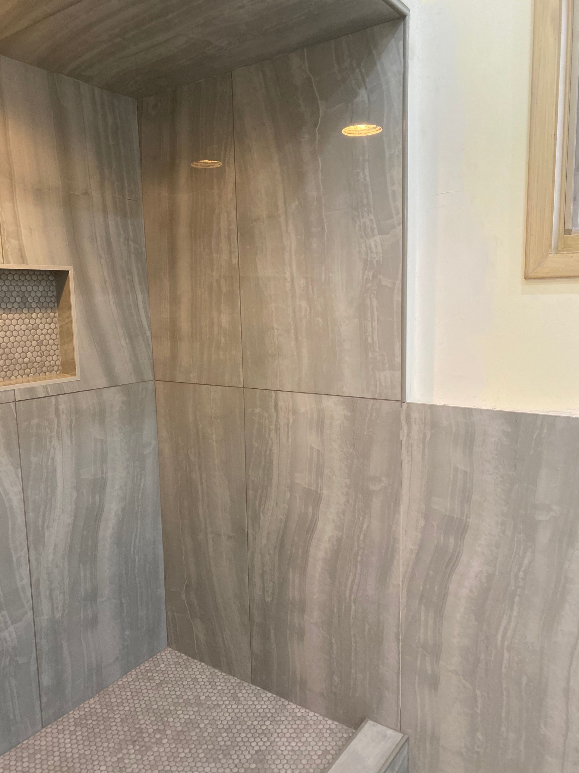 Small wood-paneled shower stall with pebble-textured floor and built-in shelf.