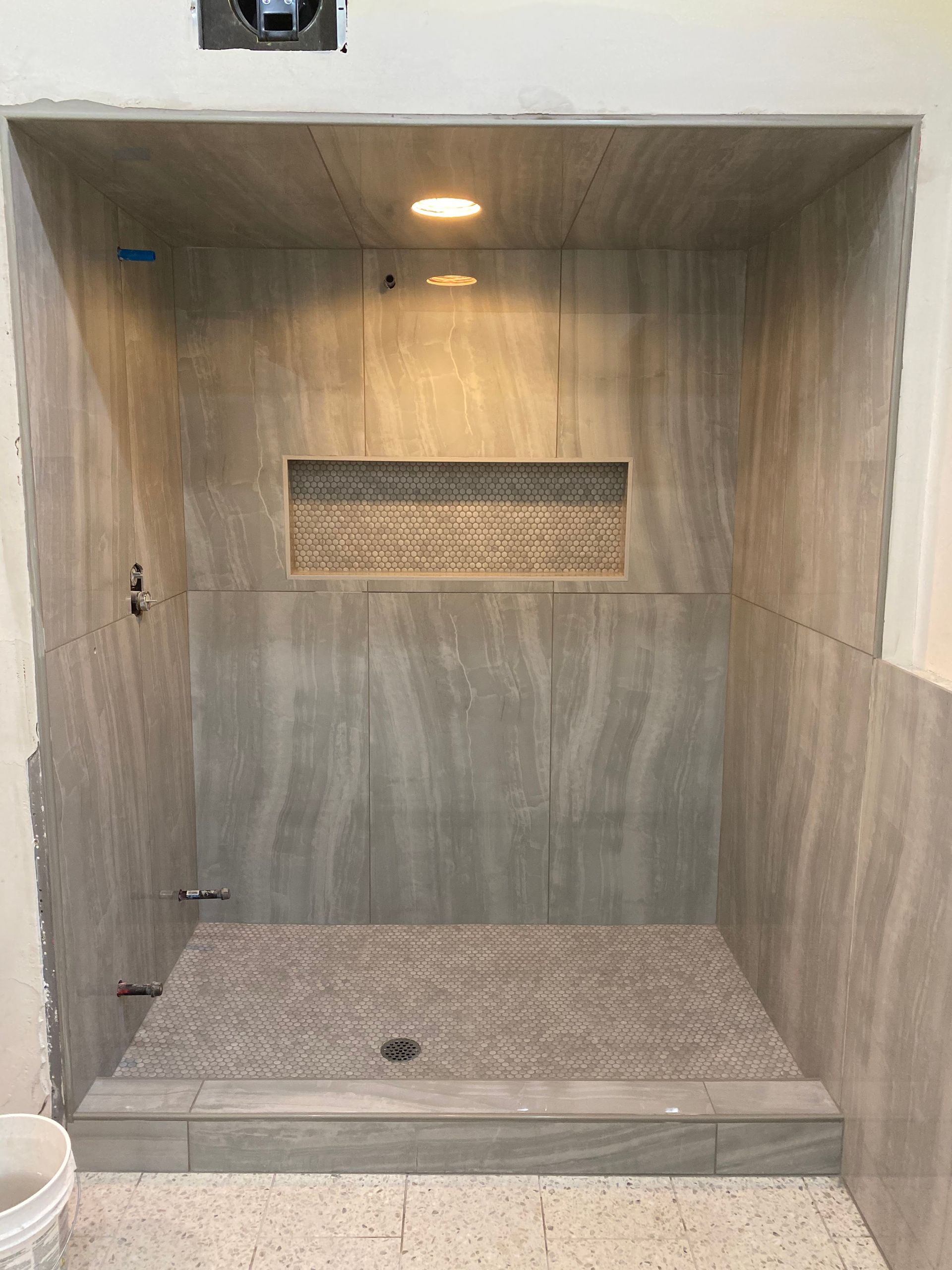 Empty tiled shower stall with a built-in bench, grab bars, and a small window.
