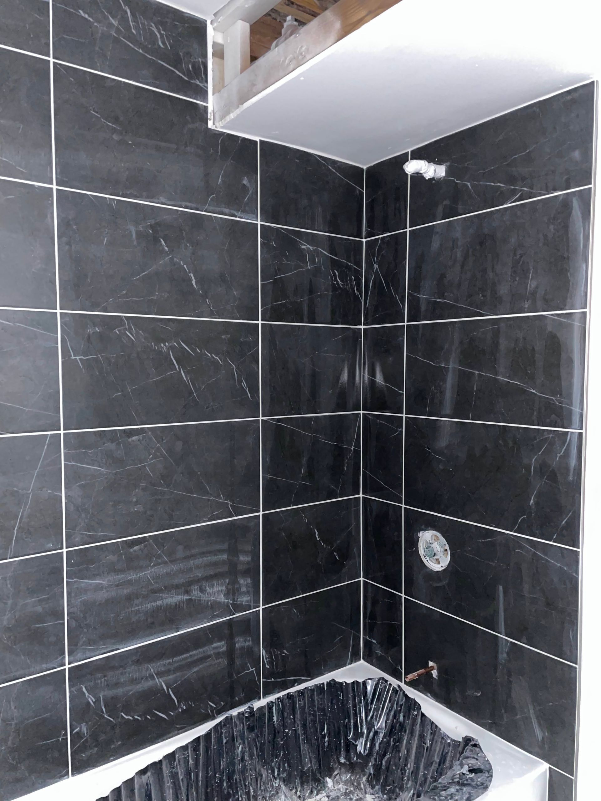 Dark tiled shower corner with a white ceiling panel and a black sink or basin at the bottom.