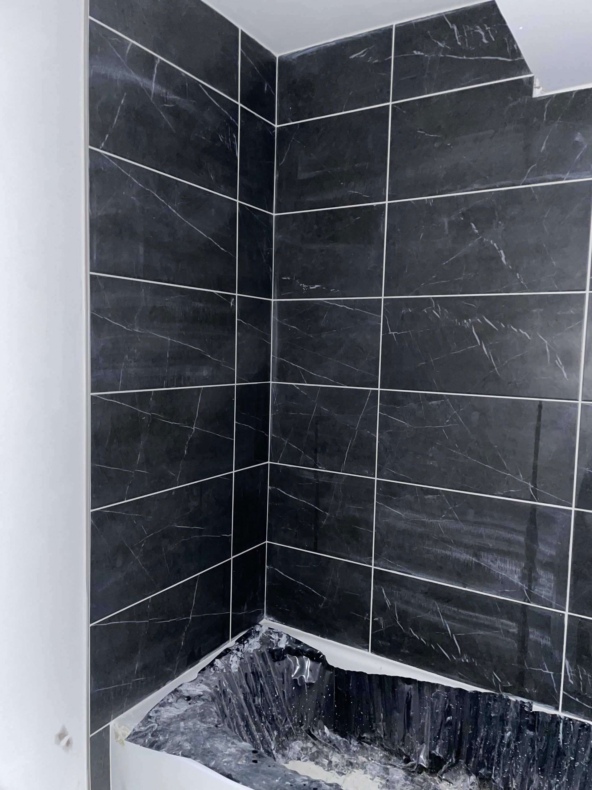 Black-tiled shower stall with a rough, unfinished shower floor and corner ledge