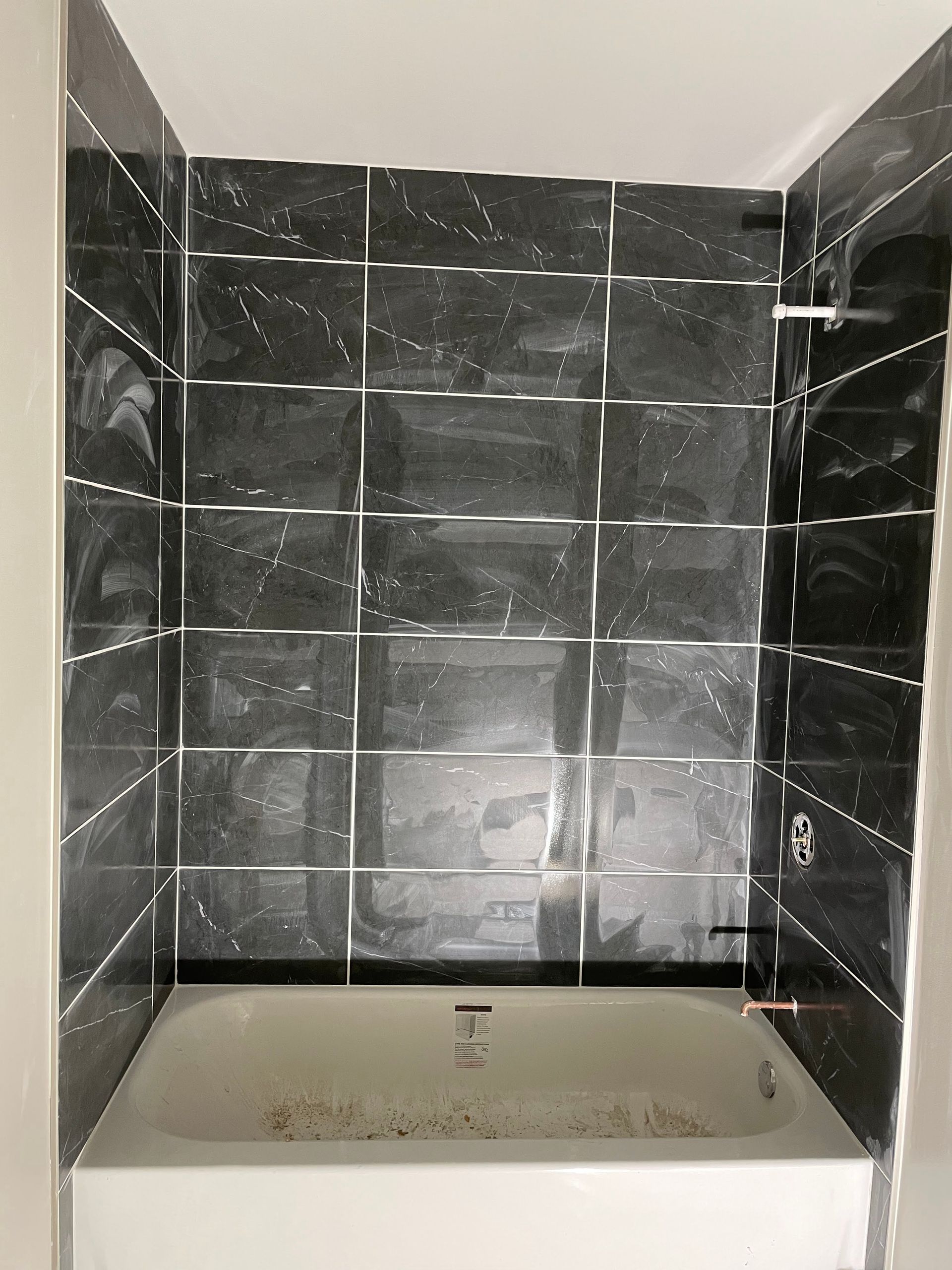 Small tiled shower alcove with a bathtub and recessed shelf, shown in dark marble-pattern tiles.