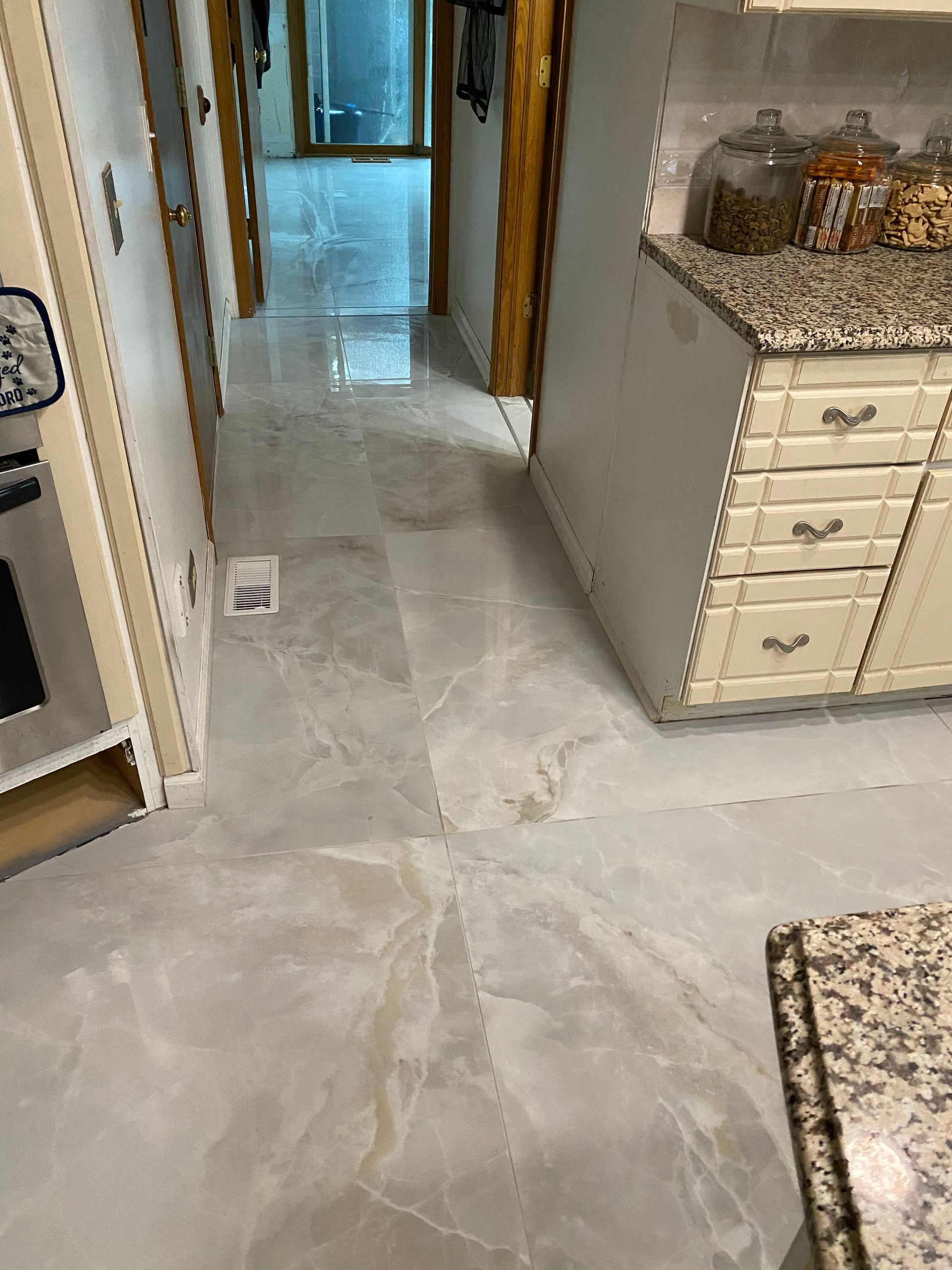 Kitchen hallway with light gray tile floor, white cabinets, and granite countertops.