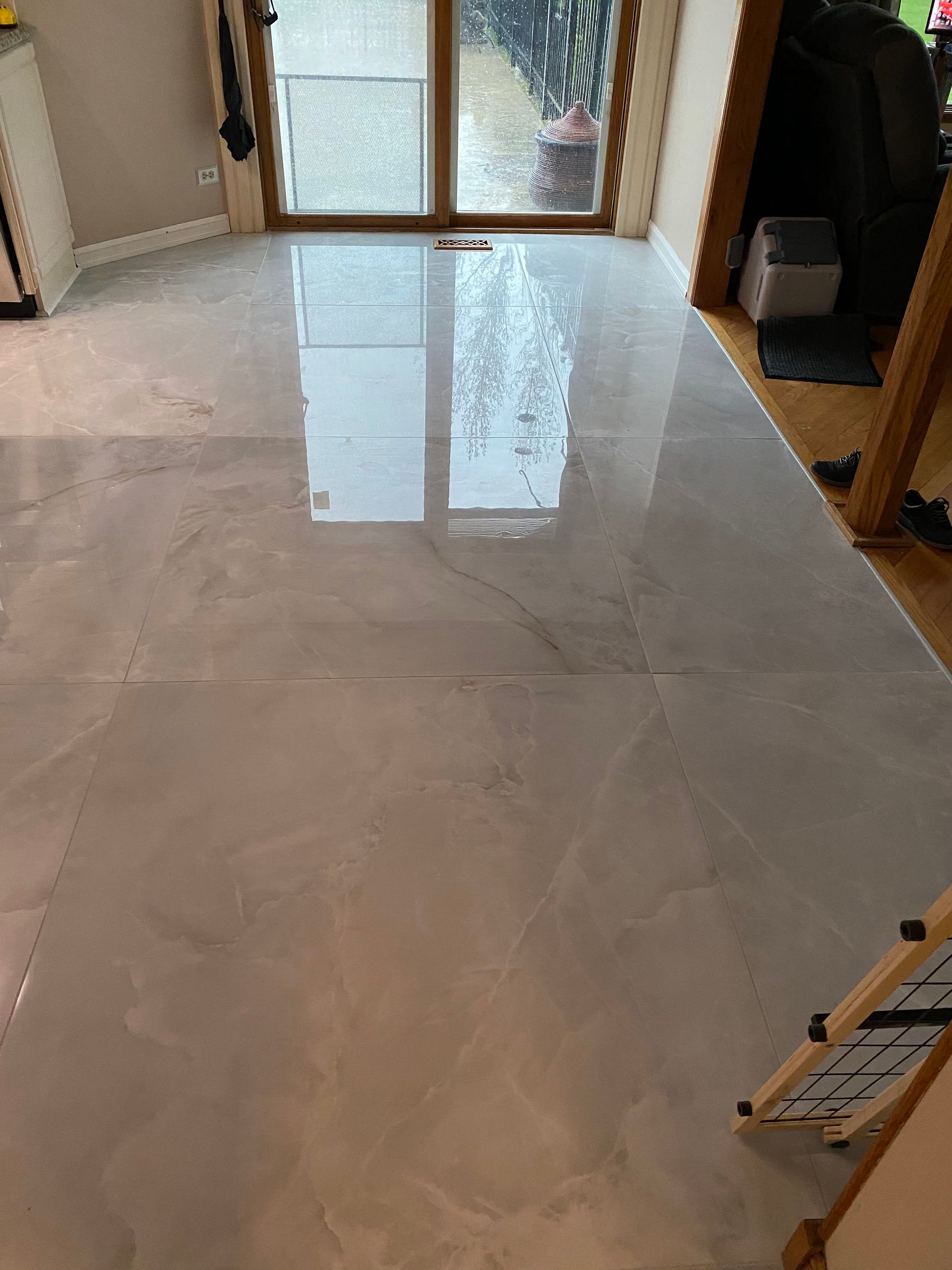 Polished light tile floor in a home hallway, reflecting a glass door at the far end.
