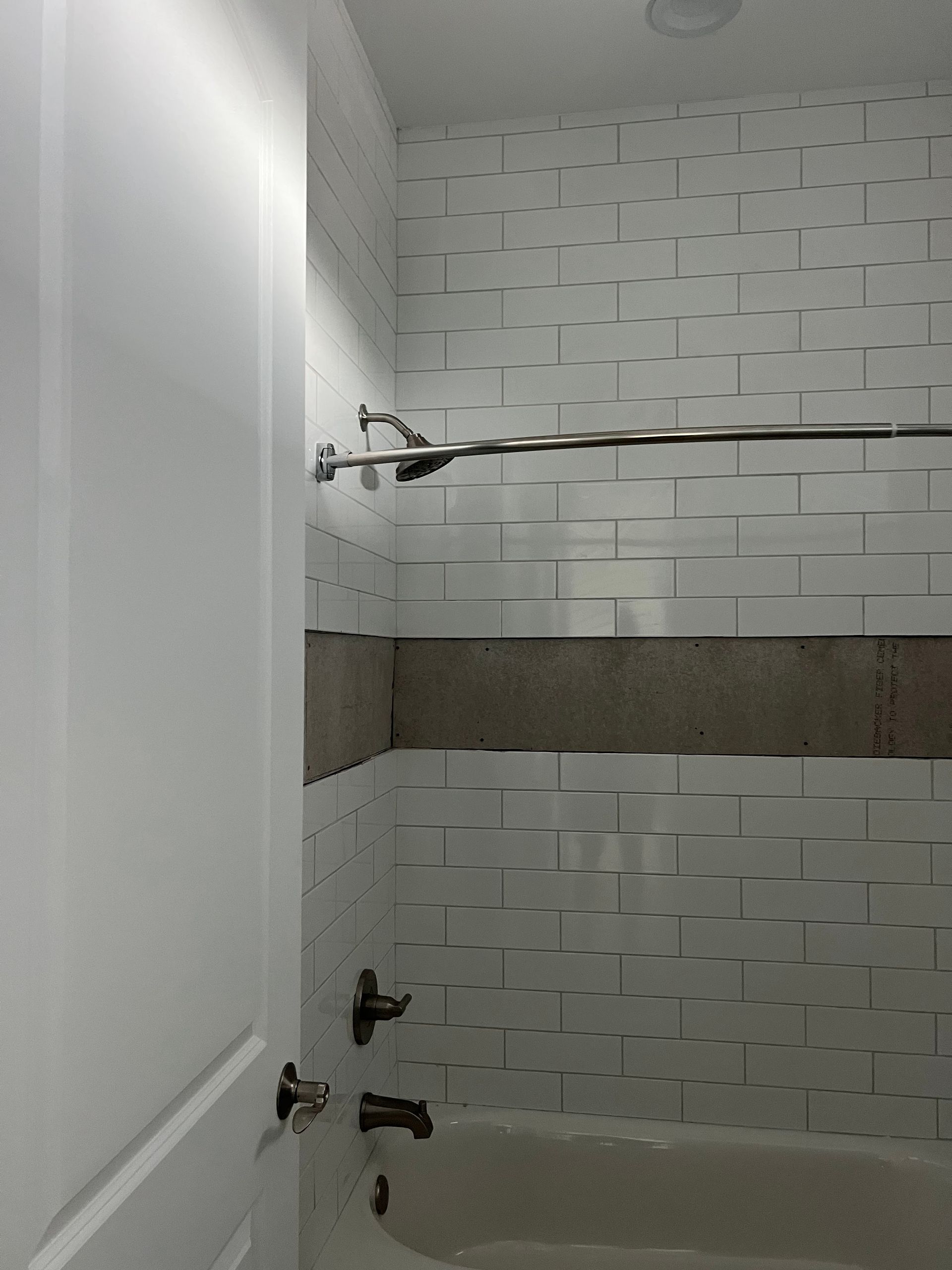 Empty tiled shower/tub area with white walls, gray accent band, and shower rod.