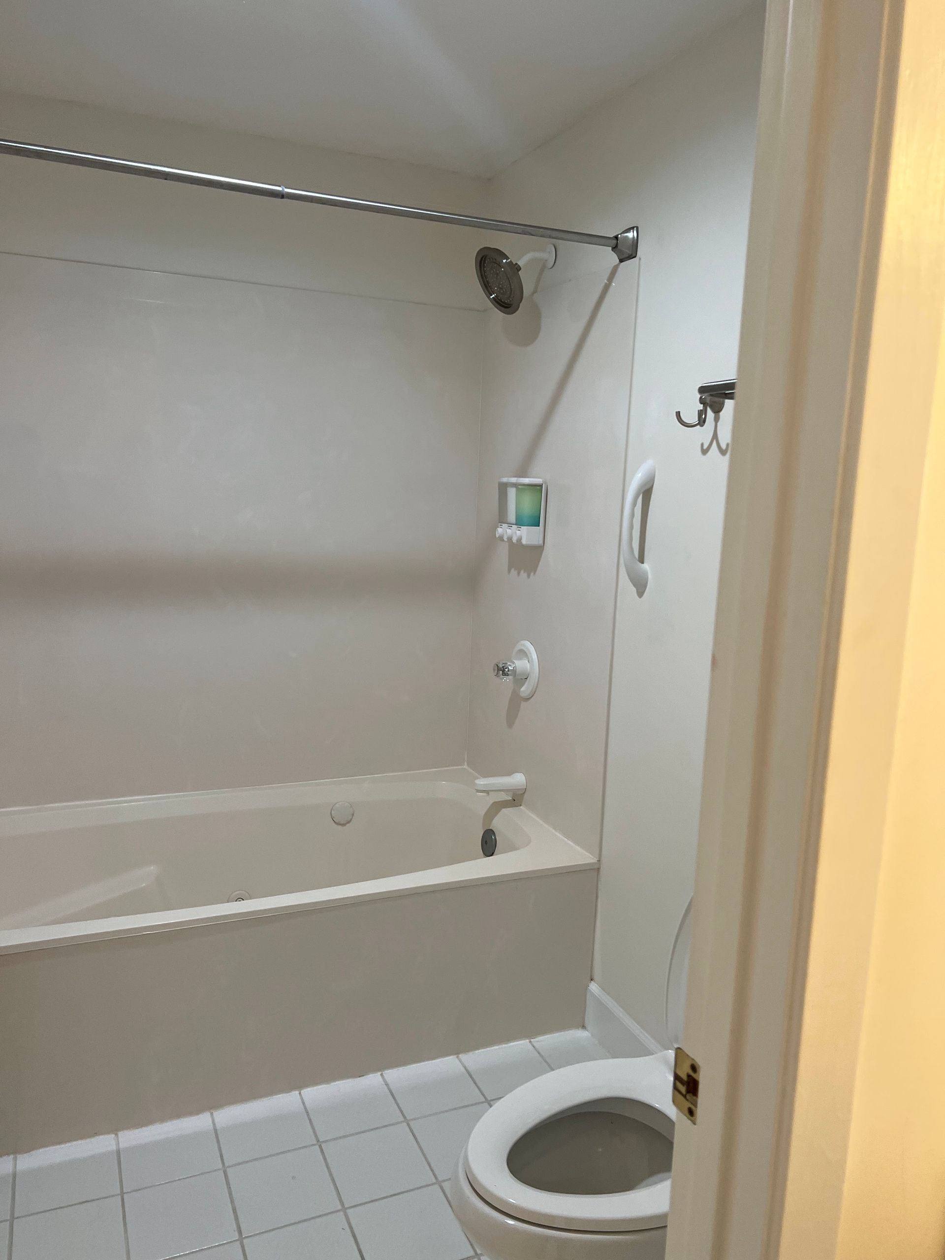 Small bathroom with bathtub, toilet, showerhead, and white tiled floor.