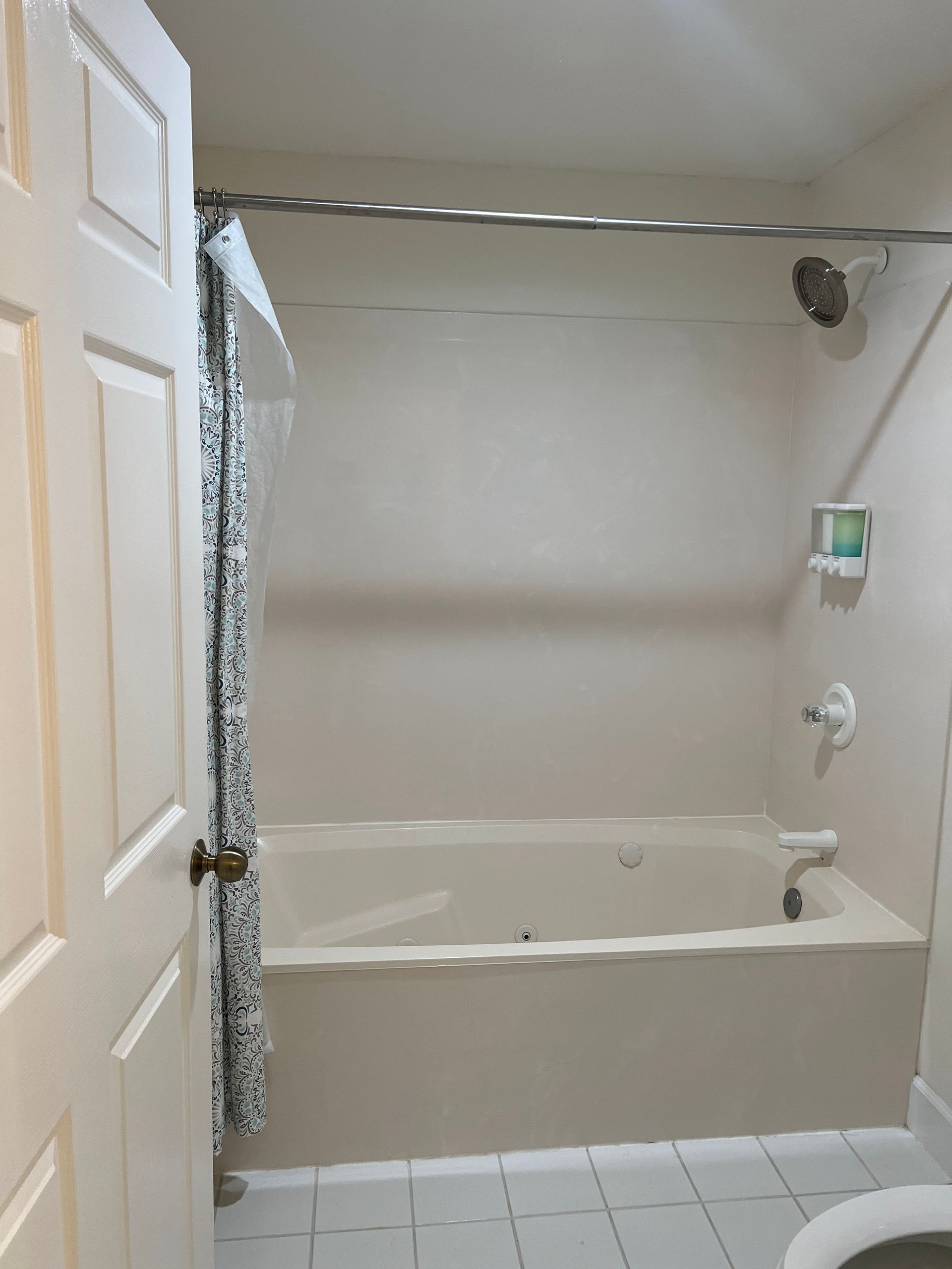Small beige bathroom with a white bathtub, tiled floor, and shower curtain.