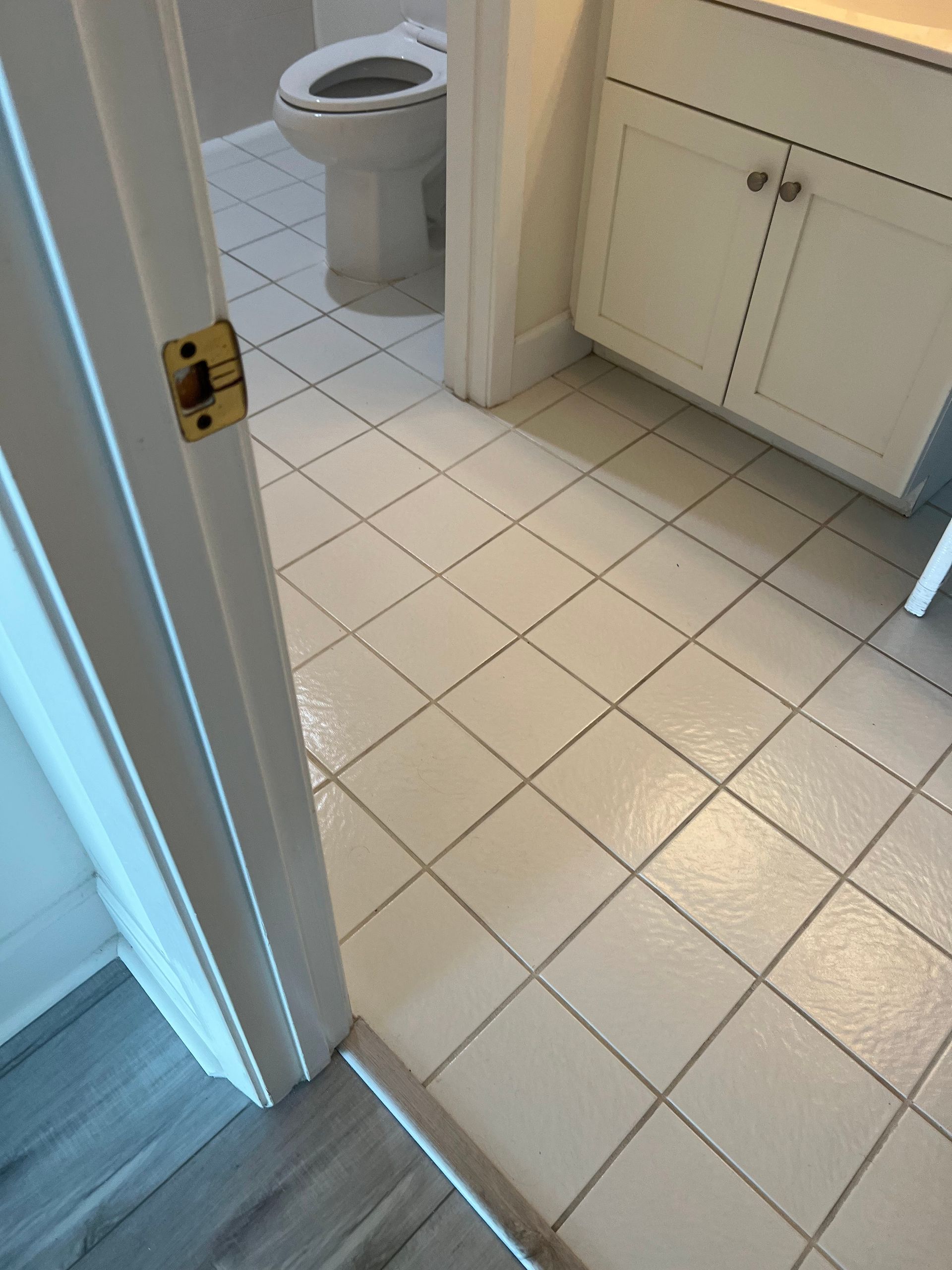 Bathroom doorway with white tiled floor, sink cabinet, and toilet visible.