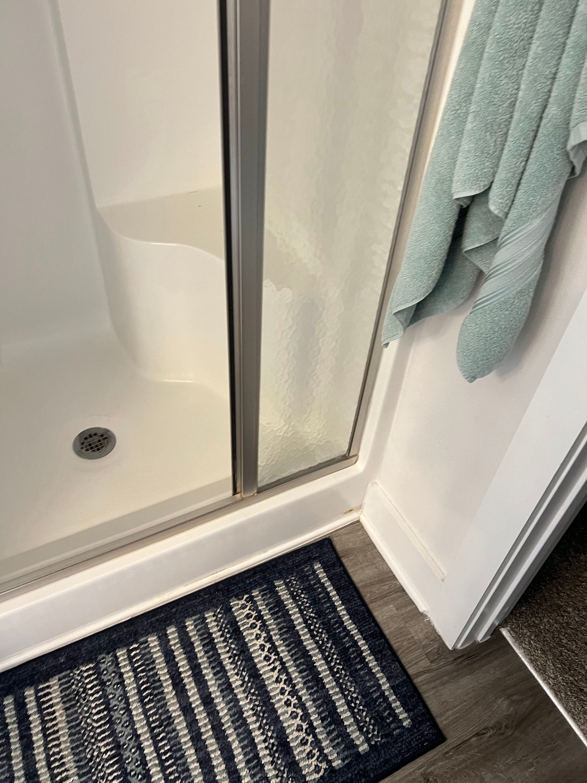 Bathroom shower with striped navy rug and hanging teal towel by a glass shower door