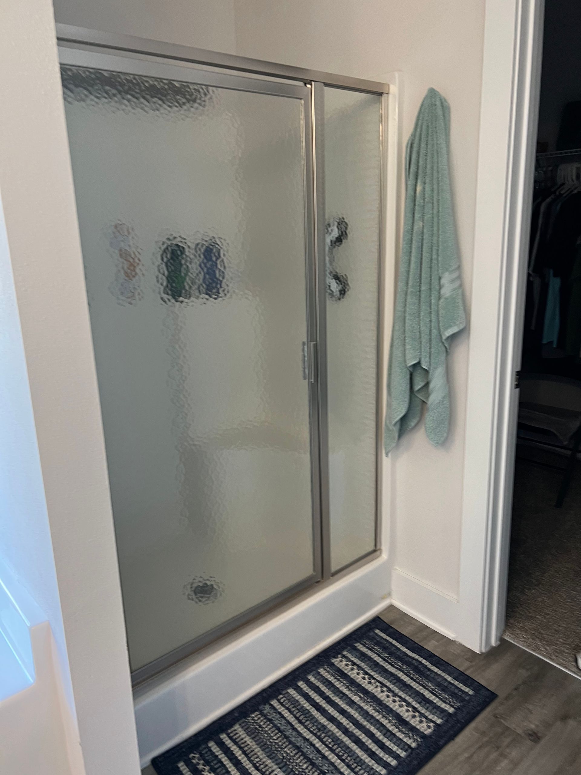Modern bathroom shower with frosted glass door, striped rug, and towel hanging on the wall