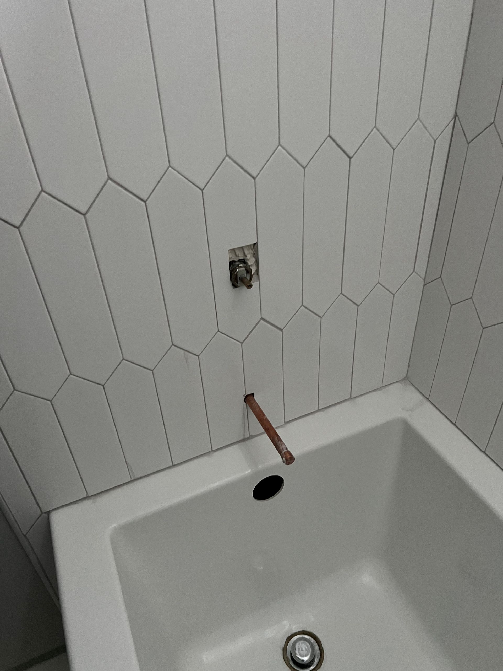 Bathroom tub wall with white tile, exposed plumbing, and a copper pipe above the bathtub drain