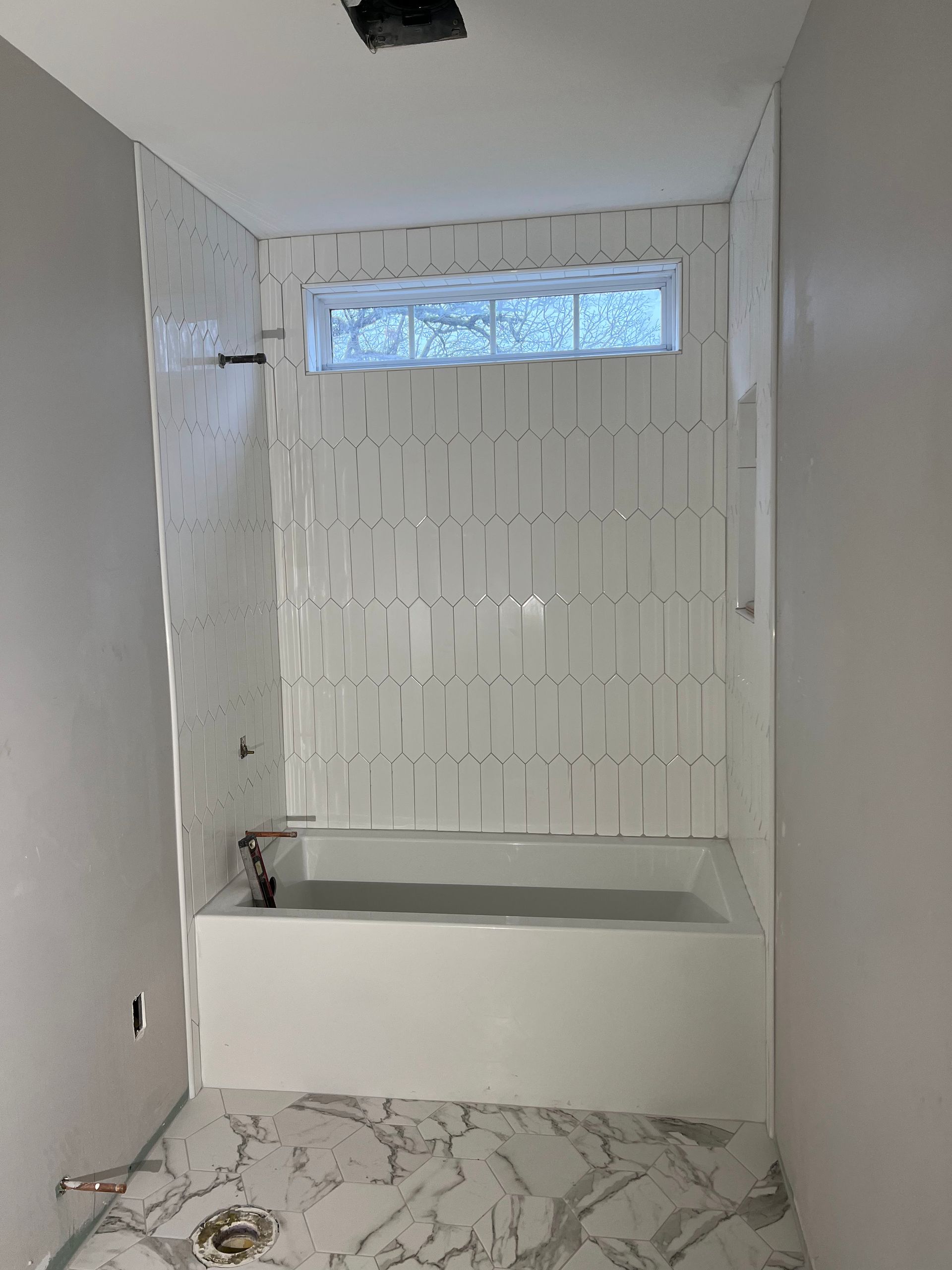 Empty bathroom under renovation with white tiled shower, tub, and marble-patterned floor