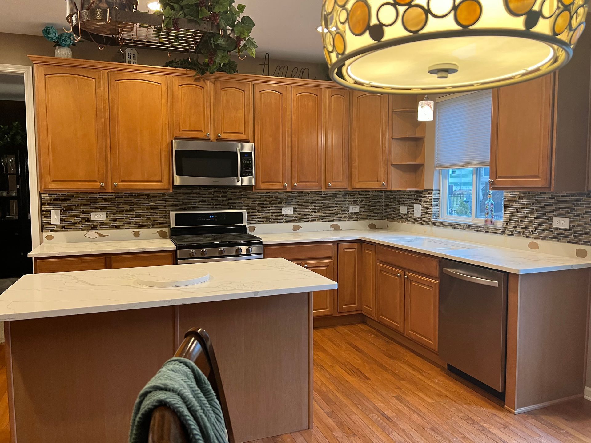 Spacious kitchen with wood cabinets, white countertops, stainless appliances, and a large hanging light fixture