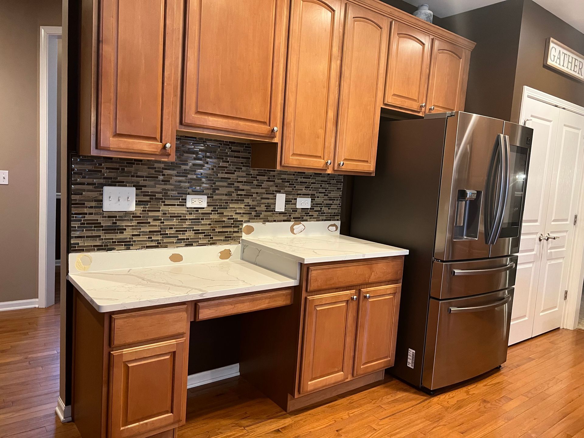 Kitchen counter with wooden cabinets, mosaic backsplash, and stainless steel refrigerator.
