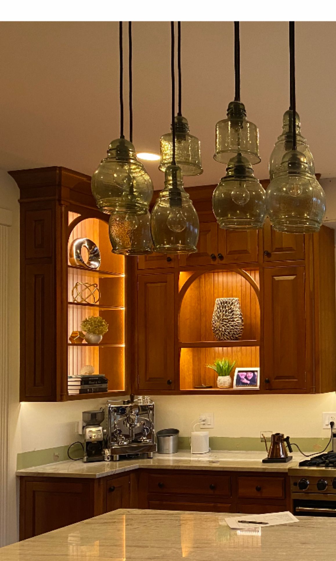 Warm kitchen with hanging glass pendant lights, wooden cabinets, and a countertop coffee maker