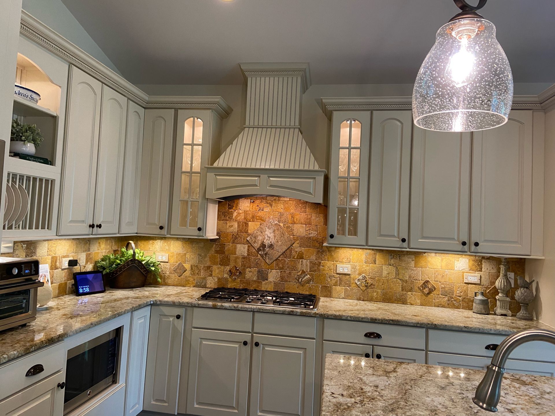 Modern kitchen with gray cabinets, marble backsplash, stone range hood, and pendant lights