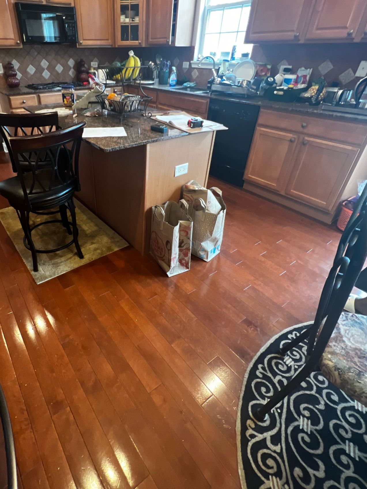 Cluttered kitchen with wooden cabinets, island, and cardboard boxes on hardwood floor