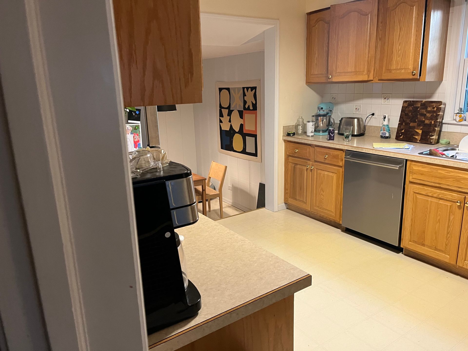 Small kitchen with wood cabinets, beige countertops, dishwasher, coffee maker, and doorway to a dining area