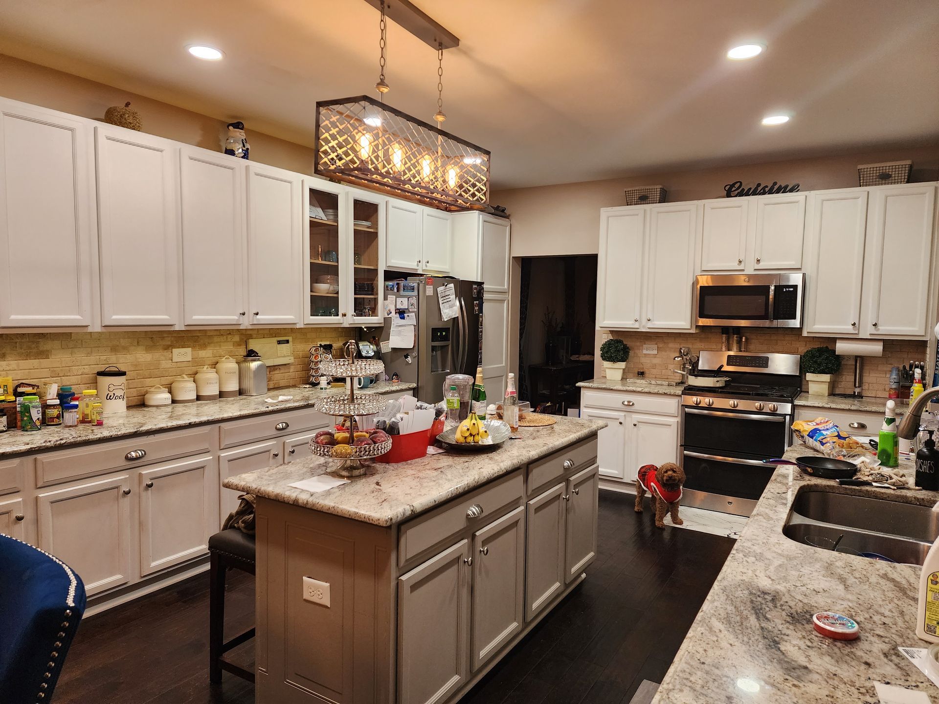 Bright modern kitchen with white cabinets, center island, and granite countertops, lit by pendant lights.