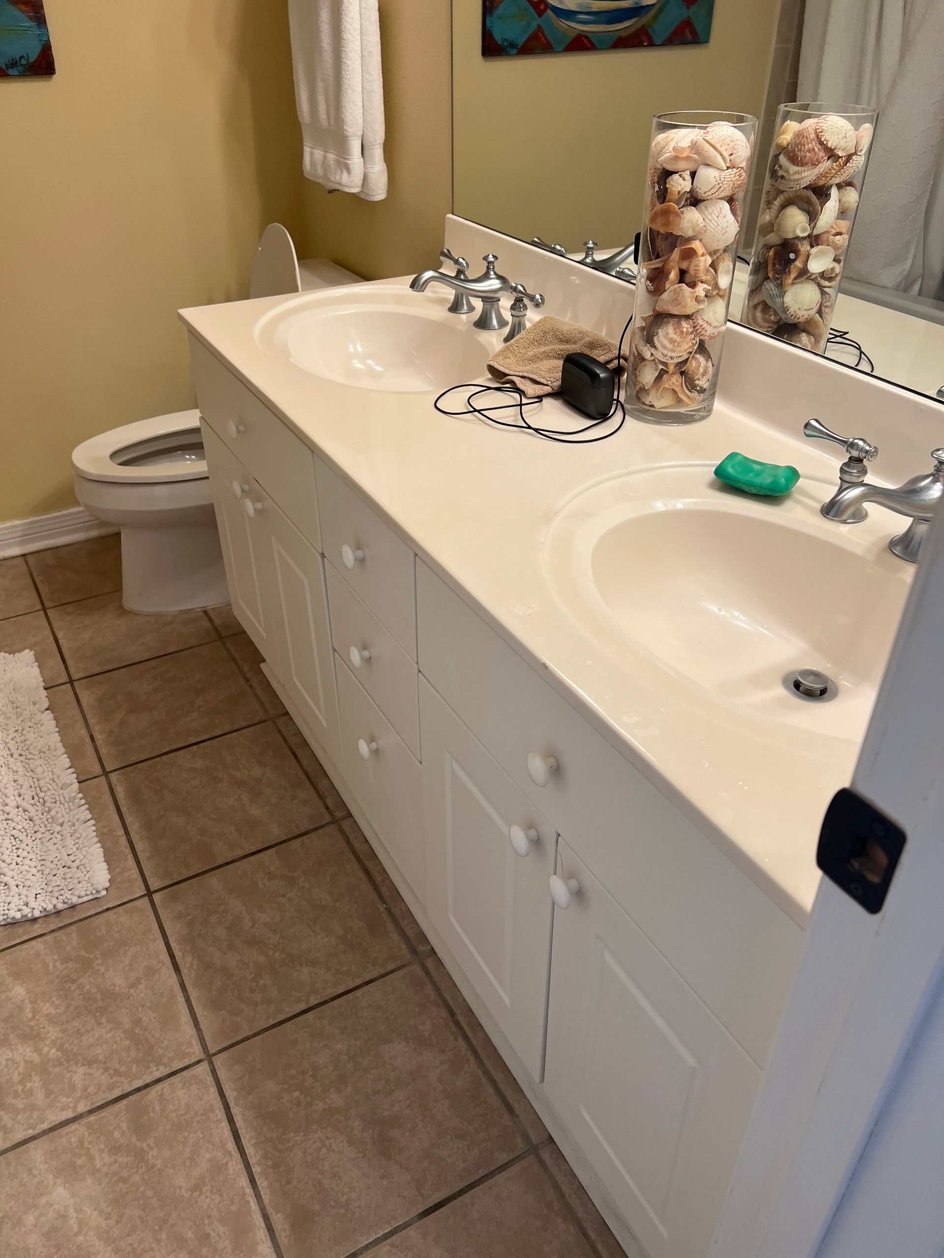 Bathroom vanity with double sinks, mirror, toilet, and tiled floor; cat figurine on the counter.