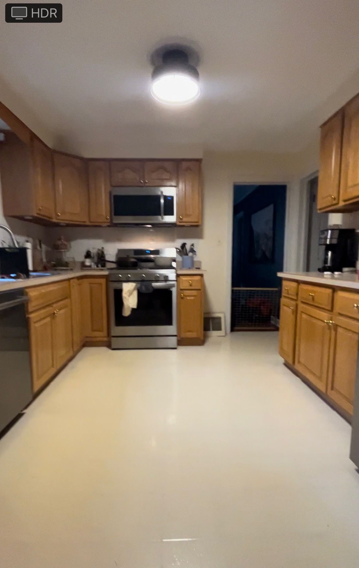 Empty kitchen with wooden cabinets, white floor, and stove under a ceiling light.