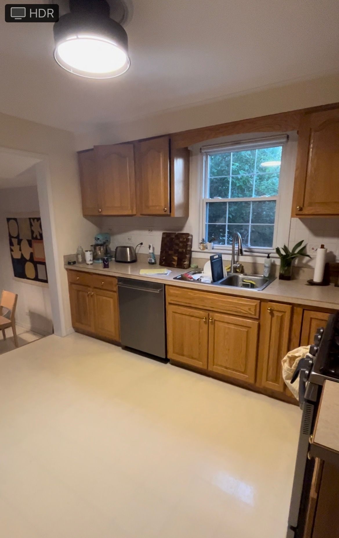 Bright kitchen with wooden cabinets, white countertops, dishwasher, sink under a window, and overhead light.