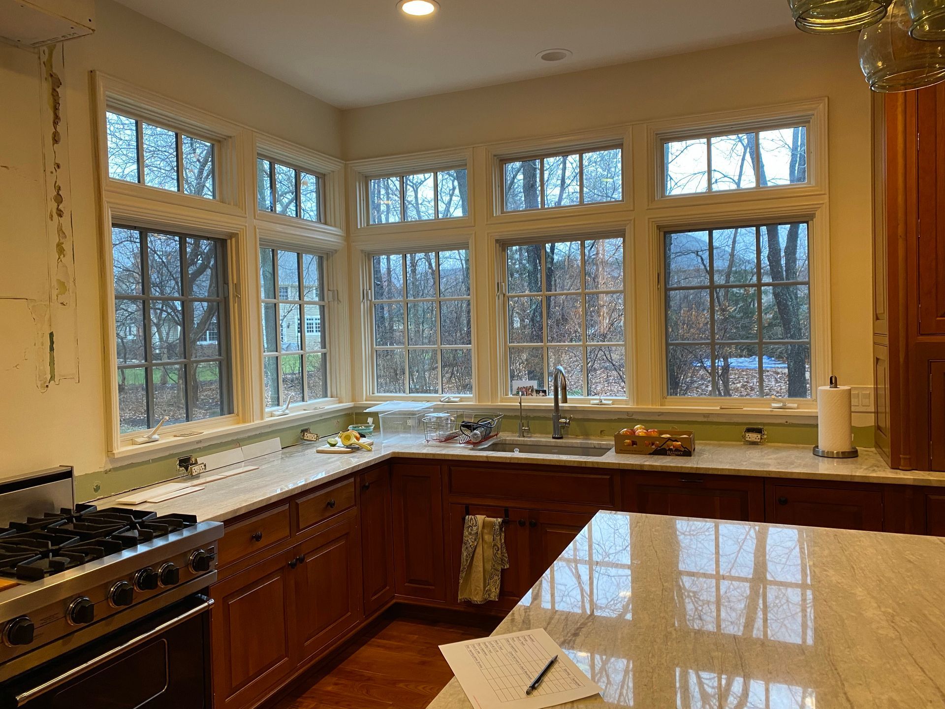 Bright kitchen with large windows, wood cabinets, granite island, and a stove by the left wall.