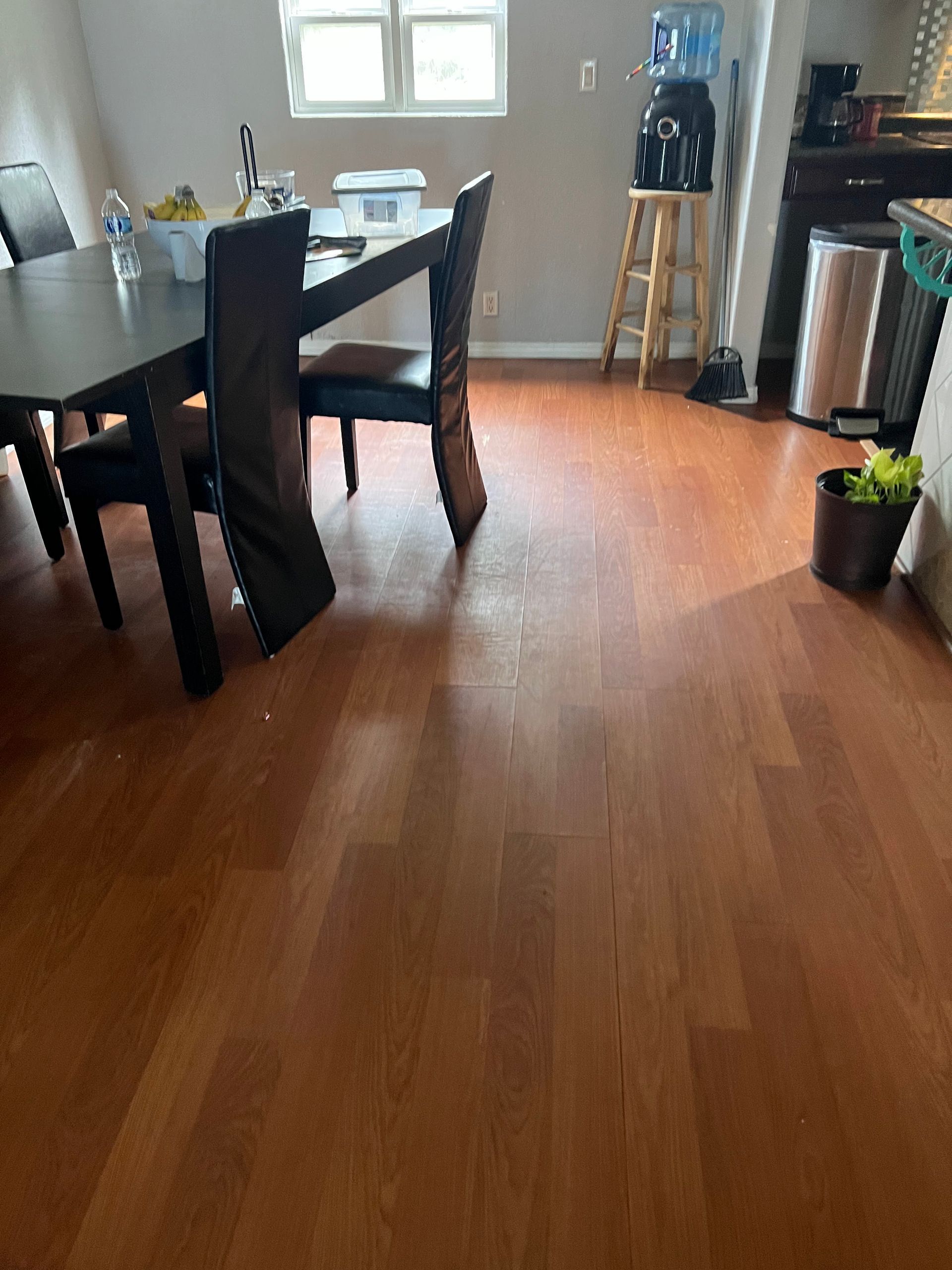 Dining room with wooden floor, dark table and chairs, window, water cooler, and potted plant.