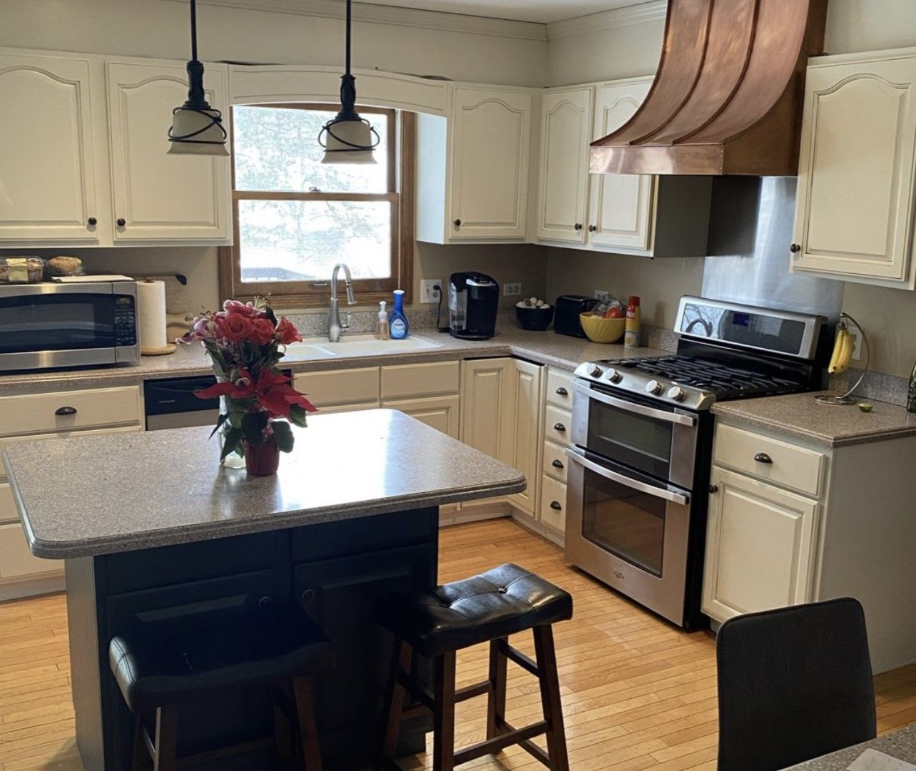 Bright kitchen with island, stainless stove, cream cabinets, and a vase of red flowers on the counter.