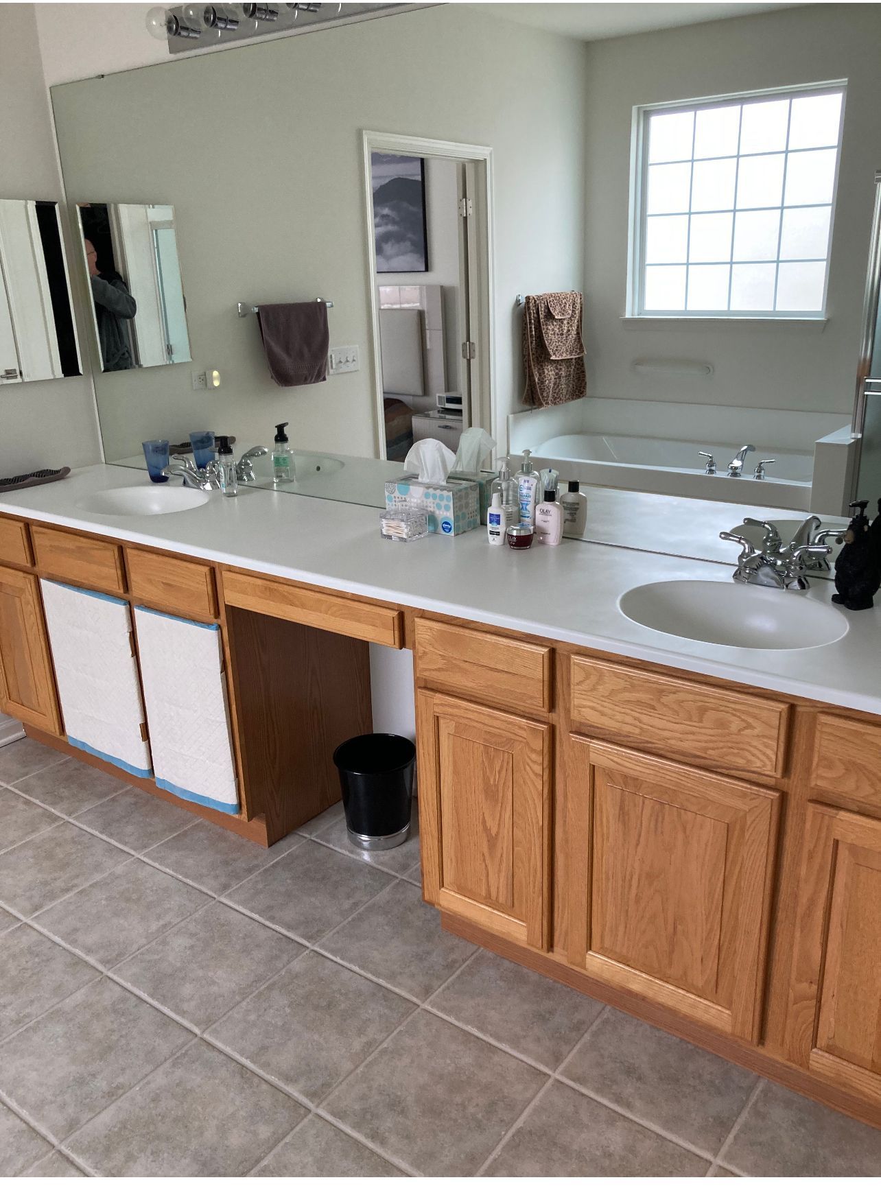 Bathroom vanity with double sinks, large mirror, wooden cabinets, and gray tile floor