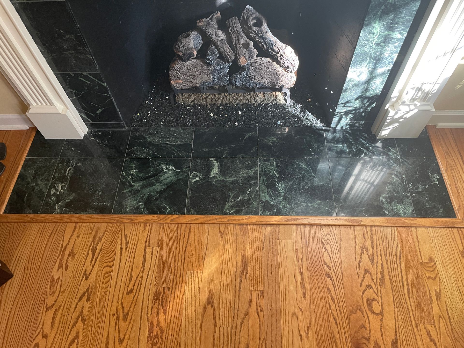 Black marble fireplace hearth with stone logs, bordered by hardwood floor and white trim.
