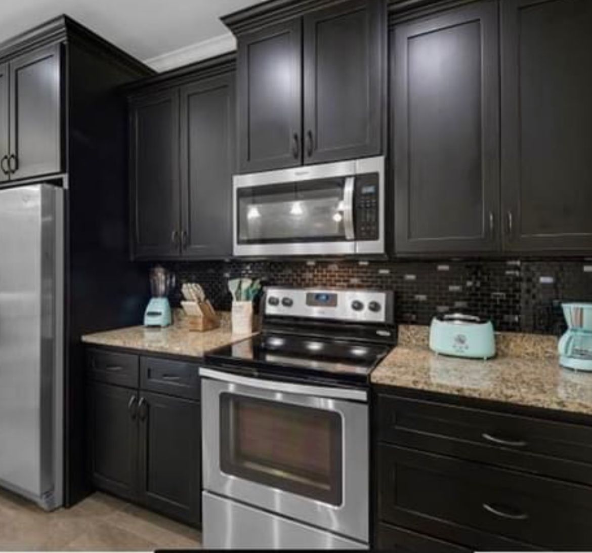 Modern kitchen with dark cabinets, stainless steel appliances, black tile backsplash, and light countertops