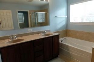 Bathroom with dark wood vanity, white sink, mirror, and bathtub beside a window.