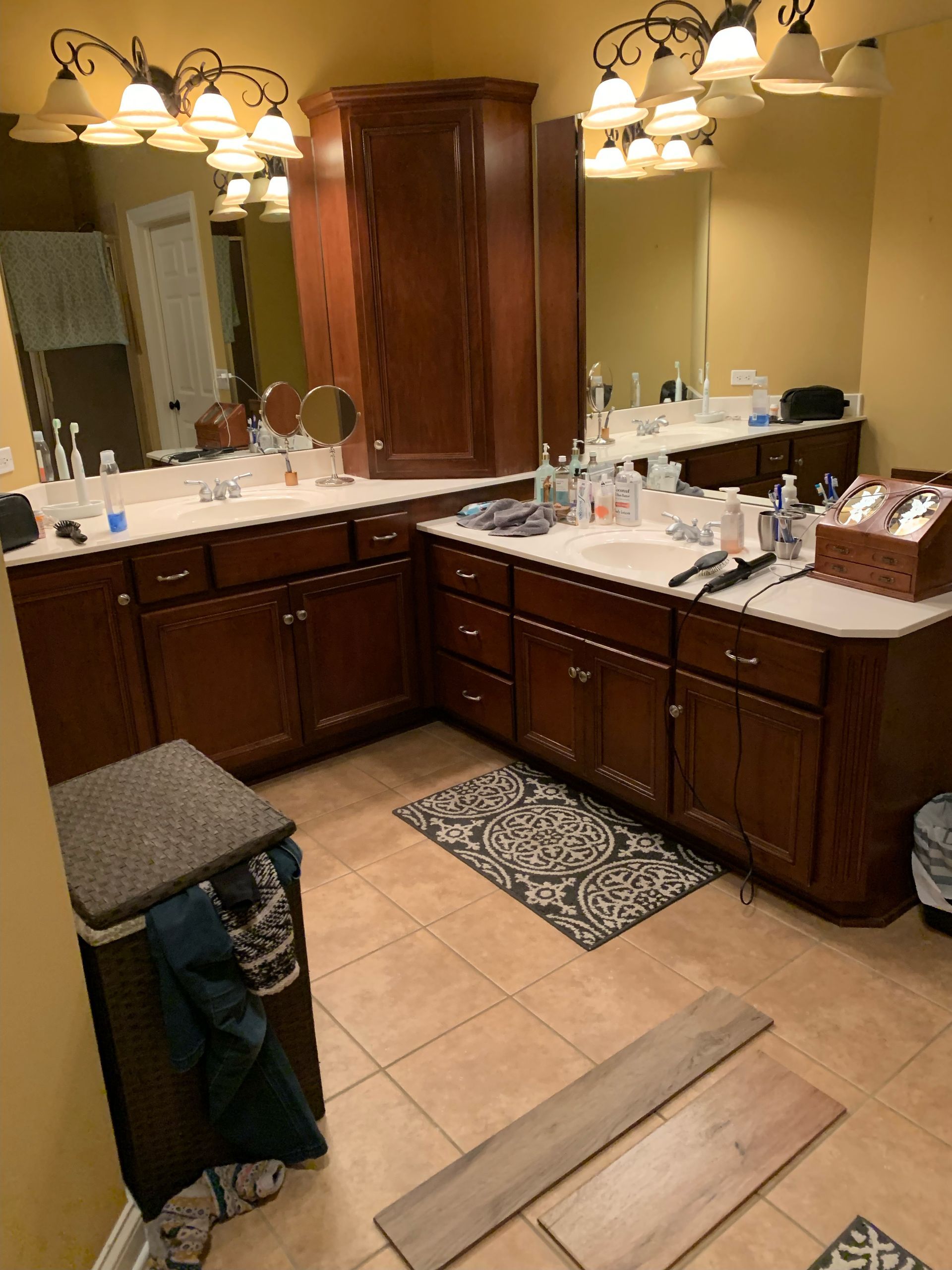 Bathroom vanity with double sinks, large mirrors, wooden cabinets, and tan tile flooring.