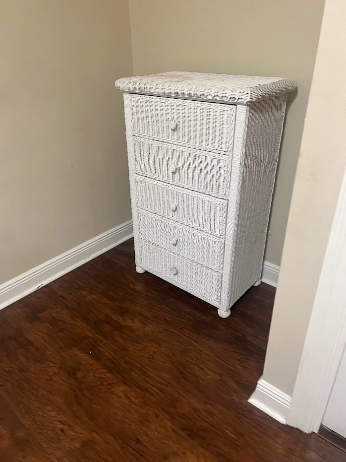 White wicker dresser in a corner of a room with wood flooring and beige walls