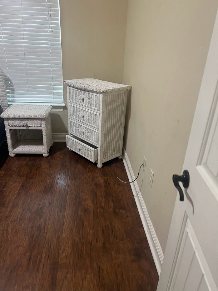 Small bedroom corner with a white wicker dresser and matching side table on dark wood flooring.