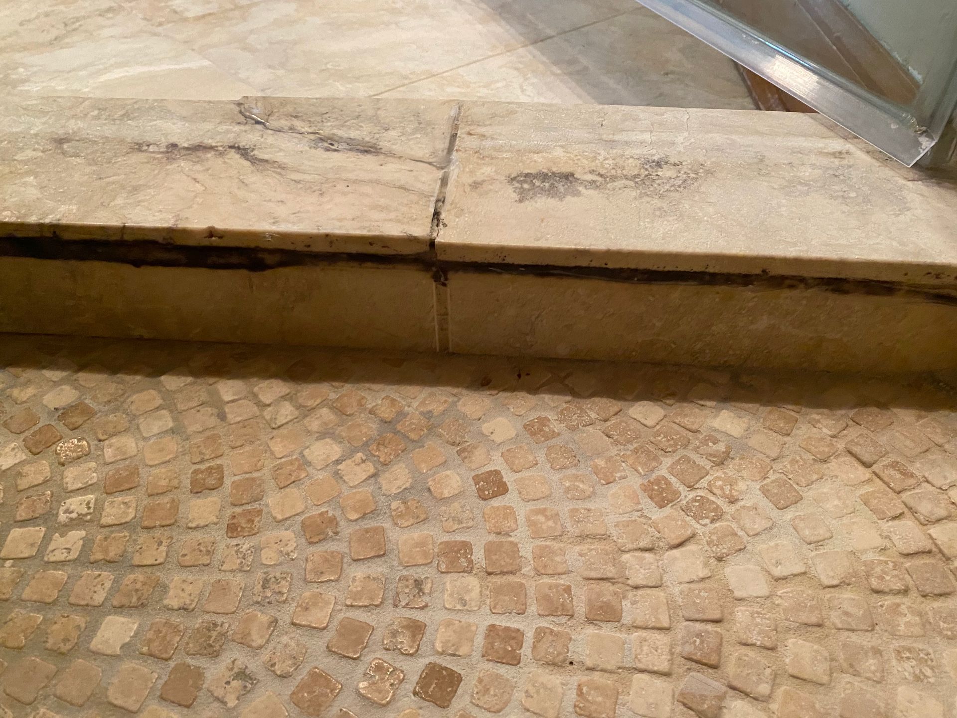 Cracked stone step above a patterned tiled floor with a metal railing at right