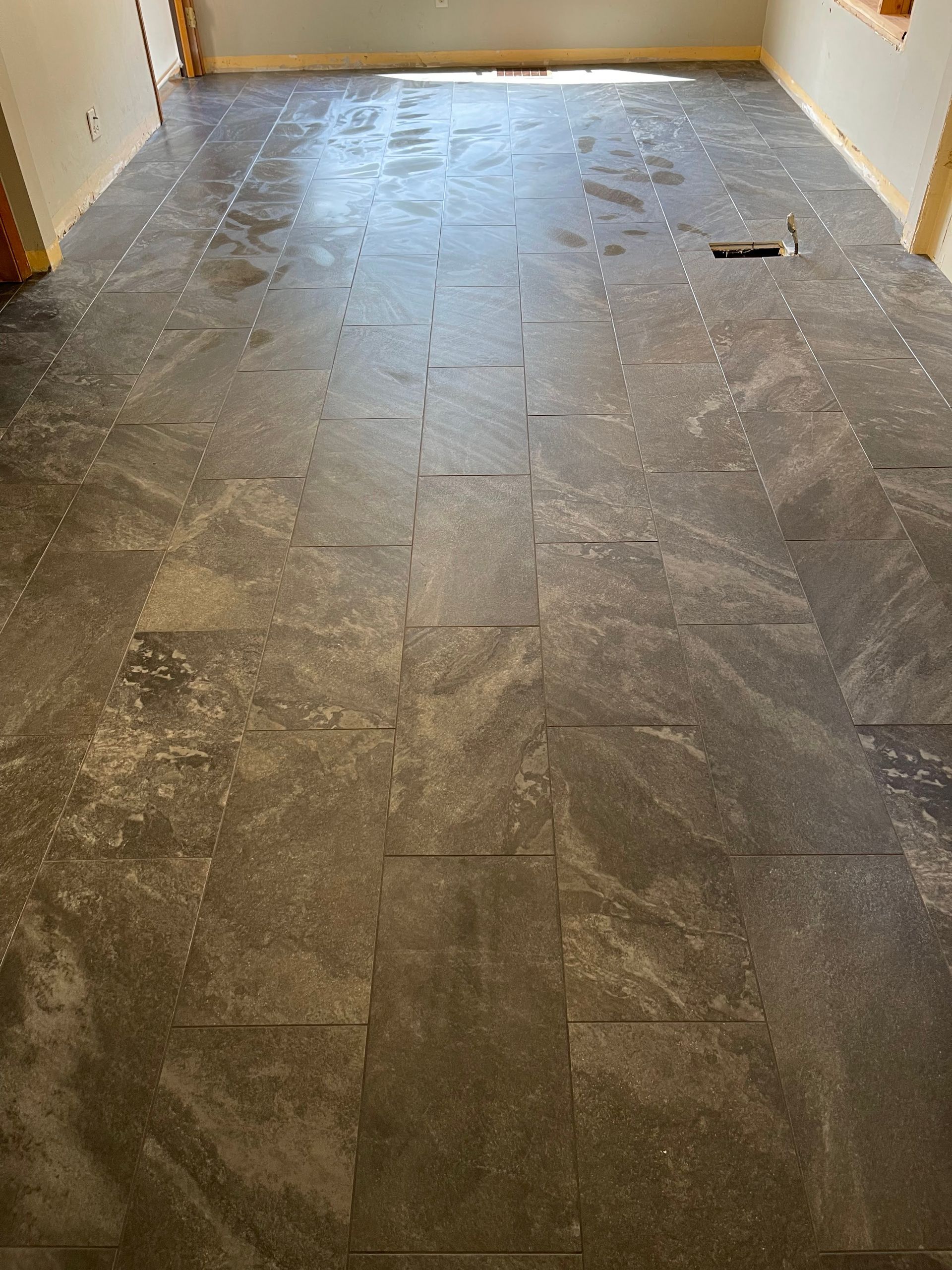 Gray stone-tile floor in an empty hallway, with a small dark object near the right wall.