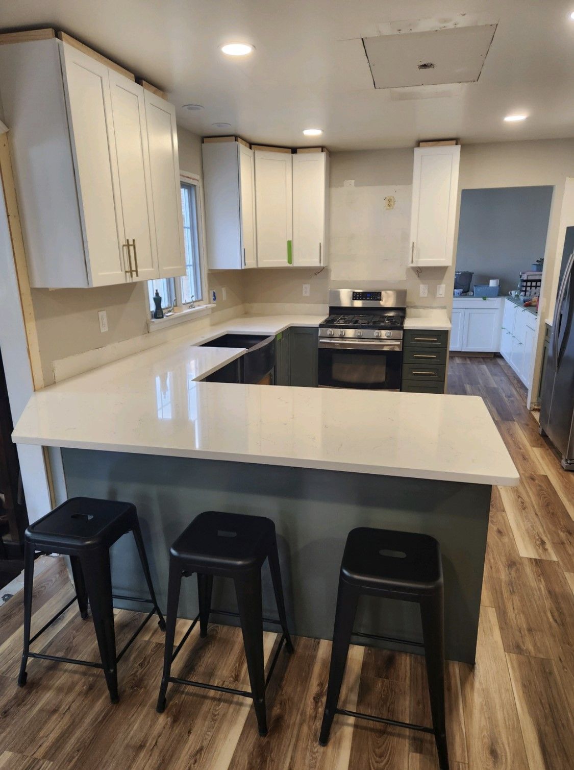 Modern kitchen with white cabinets, island counter, black stools, and wood flooring