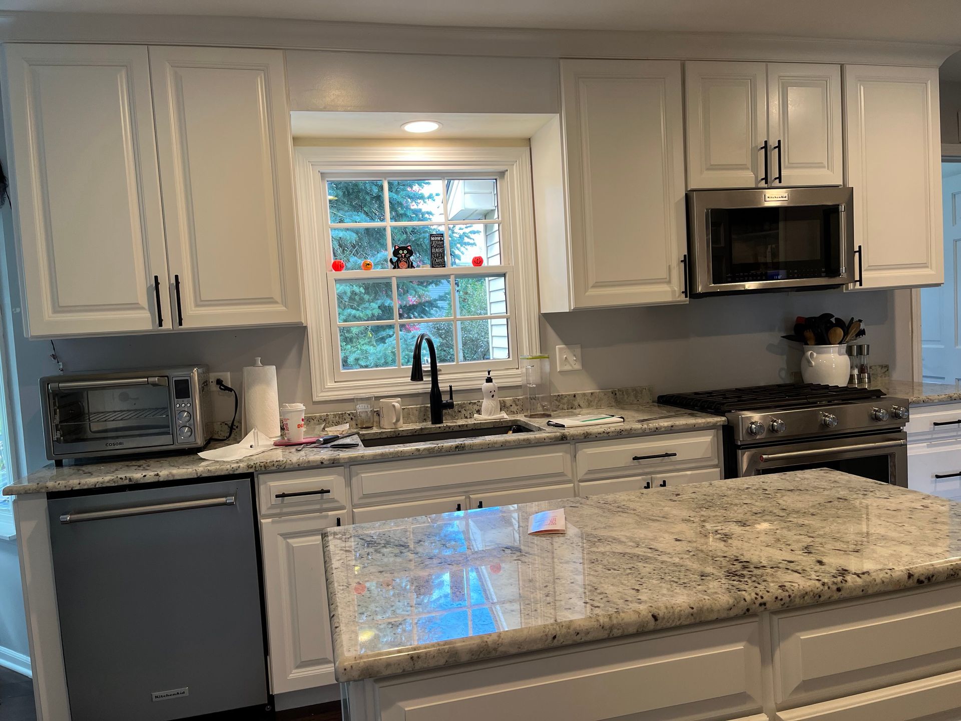 Bright kitchen with white cabinets, granite island, stainless appliances, and a window above the sink.