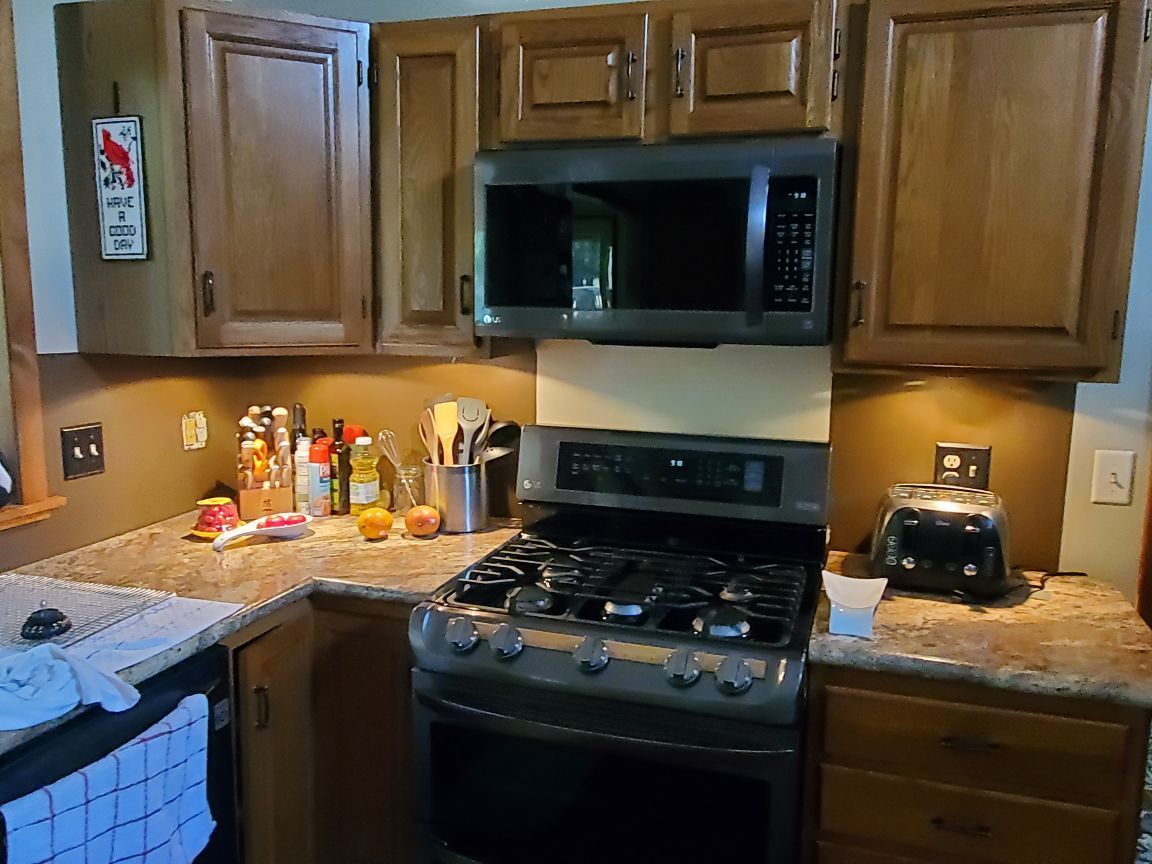Kitchen with wooden cabinets, stainless stove and microwave, and cluttered granite counters with condiments and a toaster.