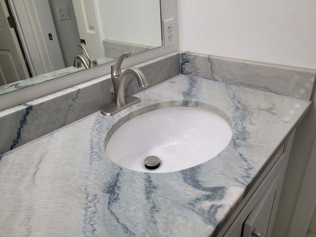 Bathroom vanity with marble countertop, oval sink, and mirror reflection