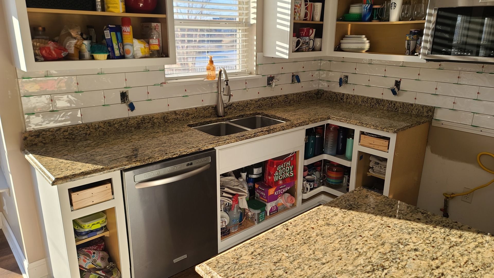 Kitchen with granite countertops, stainless dishwasher, white tile backsplash, and open shelves with storage bins.