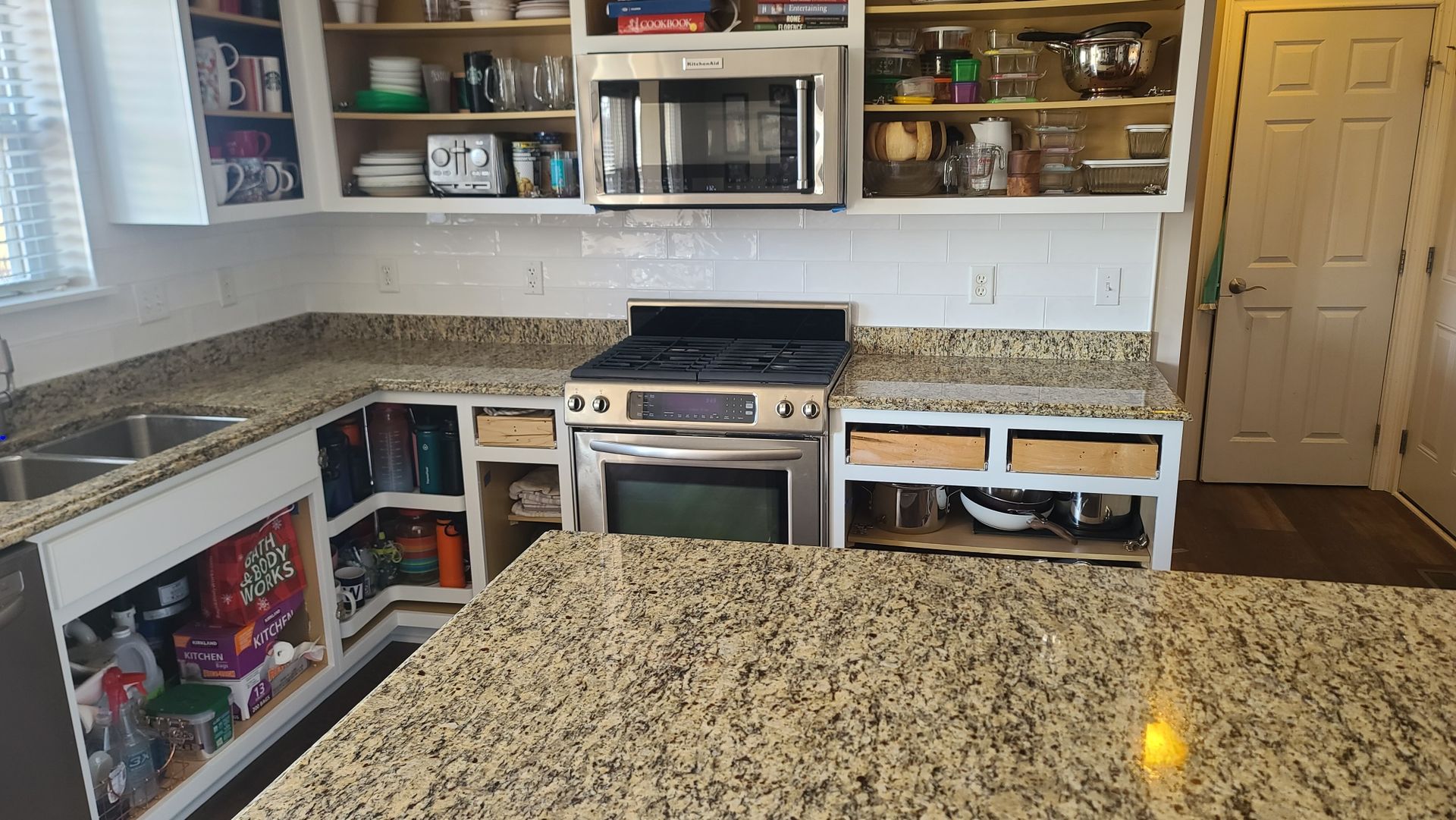 Modern kitchen with granite counters, white cabinets, stainless stove, microwave, and an island in front