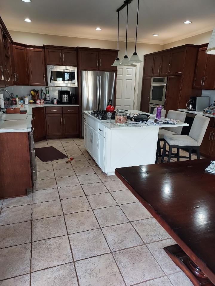 Spacious kitchen with dark wood cabinets, stainless steel fridge, and white island under pendant lights.