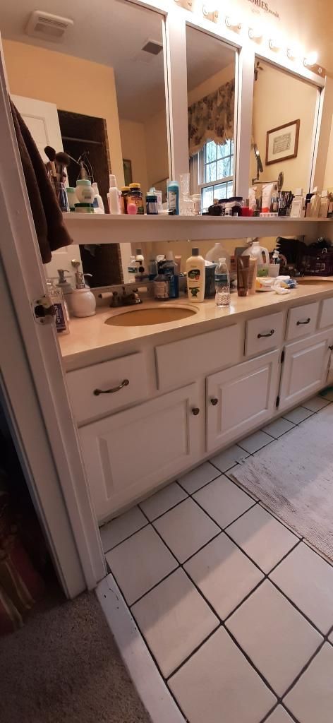 Bathroom vanity with lit mirrors, double sinks, and white tile floor