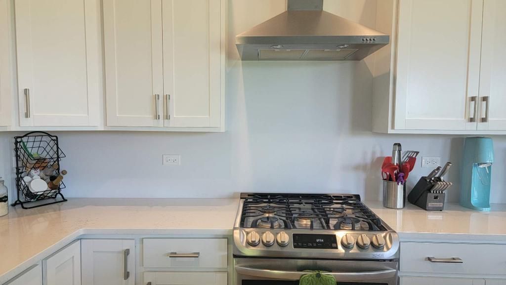 Bright white kitchen with stainless steel stove, hood, cabinets, and countertop utensil holders.